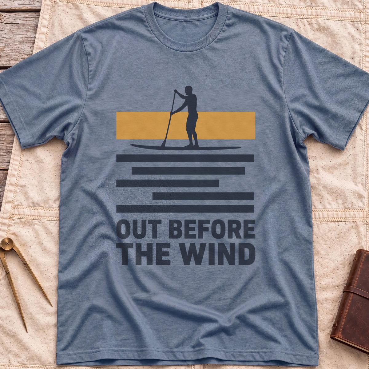 Front view of the heather indigo Out Before the Wind T-Shirt with a paddleboarder silhouetted against a tan band above striped water and the words Out Before the Wind.