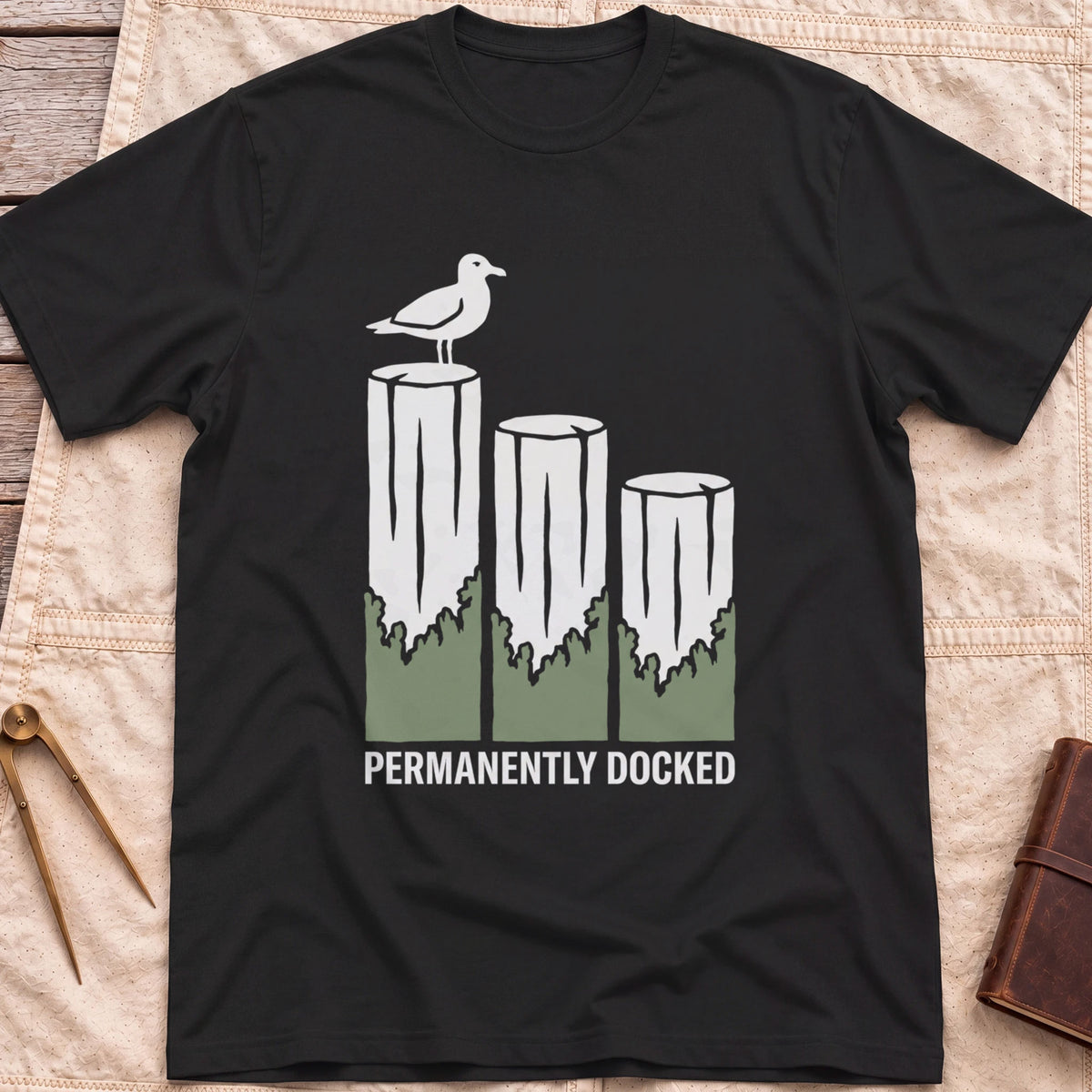 Front view of the black Permanently Docked T-Shirt with a seagull perched on three wooden pilings.