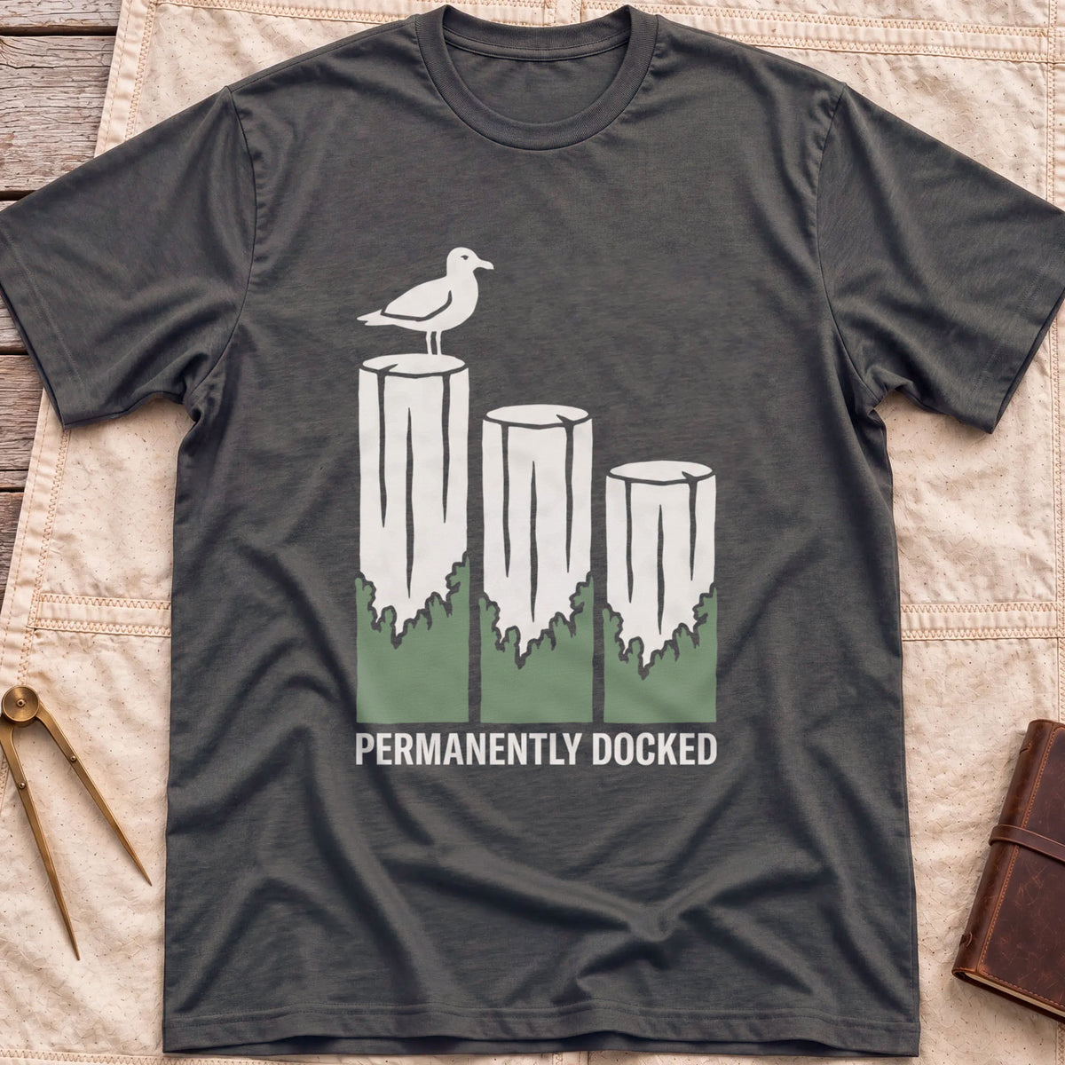 Front view of the dark heather Permanently Docked T-Shirt with a seagull perched on three wooden pilings.