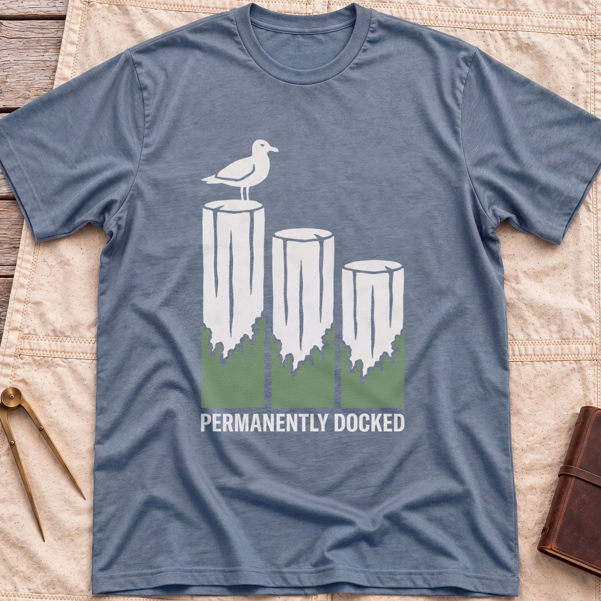 Front view of the heather indigo Permanently Docked T-Shirt with a seagull perched on three wooden pilings.