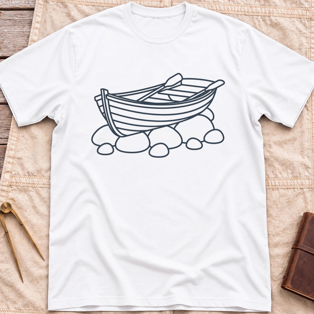 Front view of the white Pulled Ashore T-Shirt with a line drawing of a rowing boat with oars, resting on rocks.