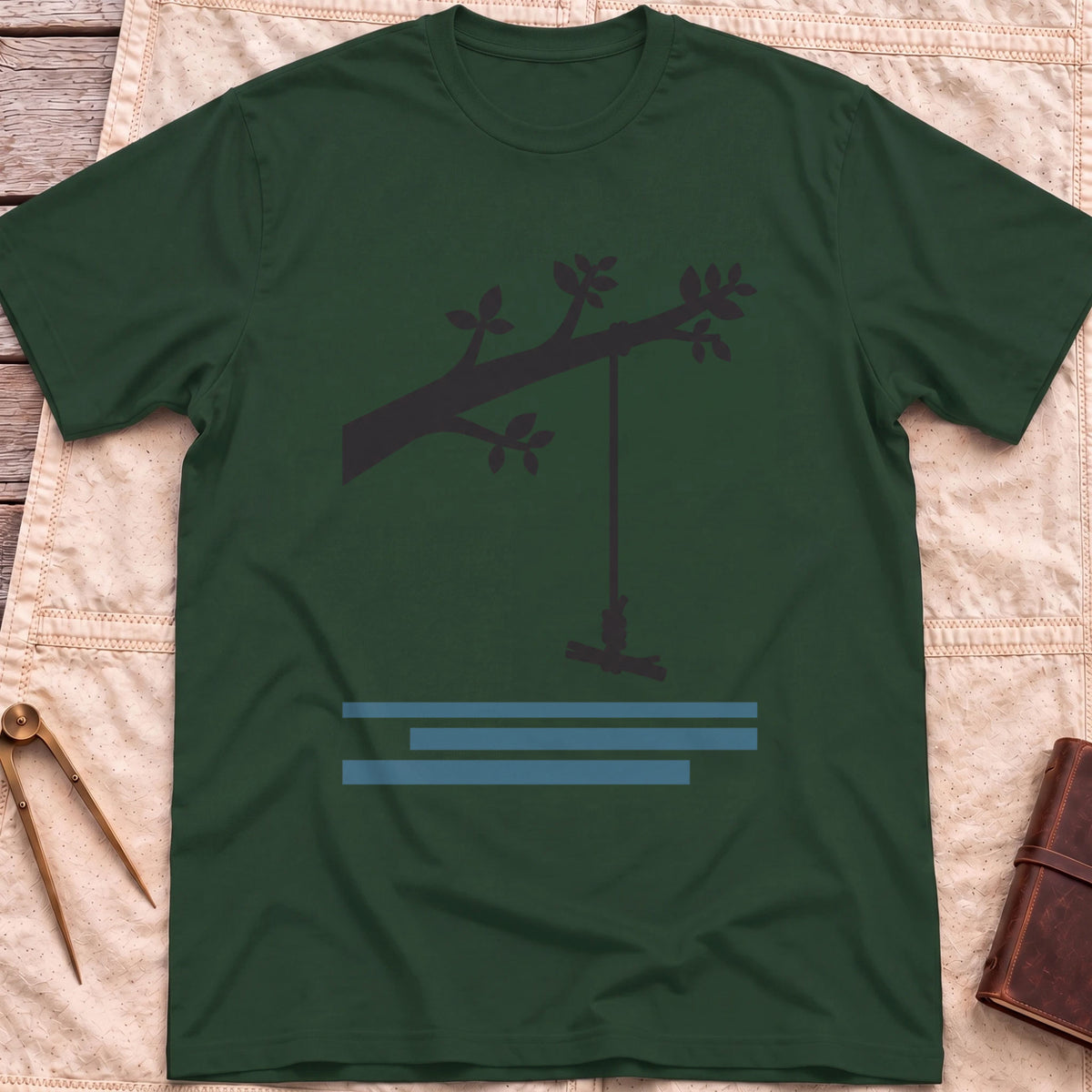 Front view of the forest green Rope Swing T-Shirt with a rope swing hanging from a leafy branch above water lines.