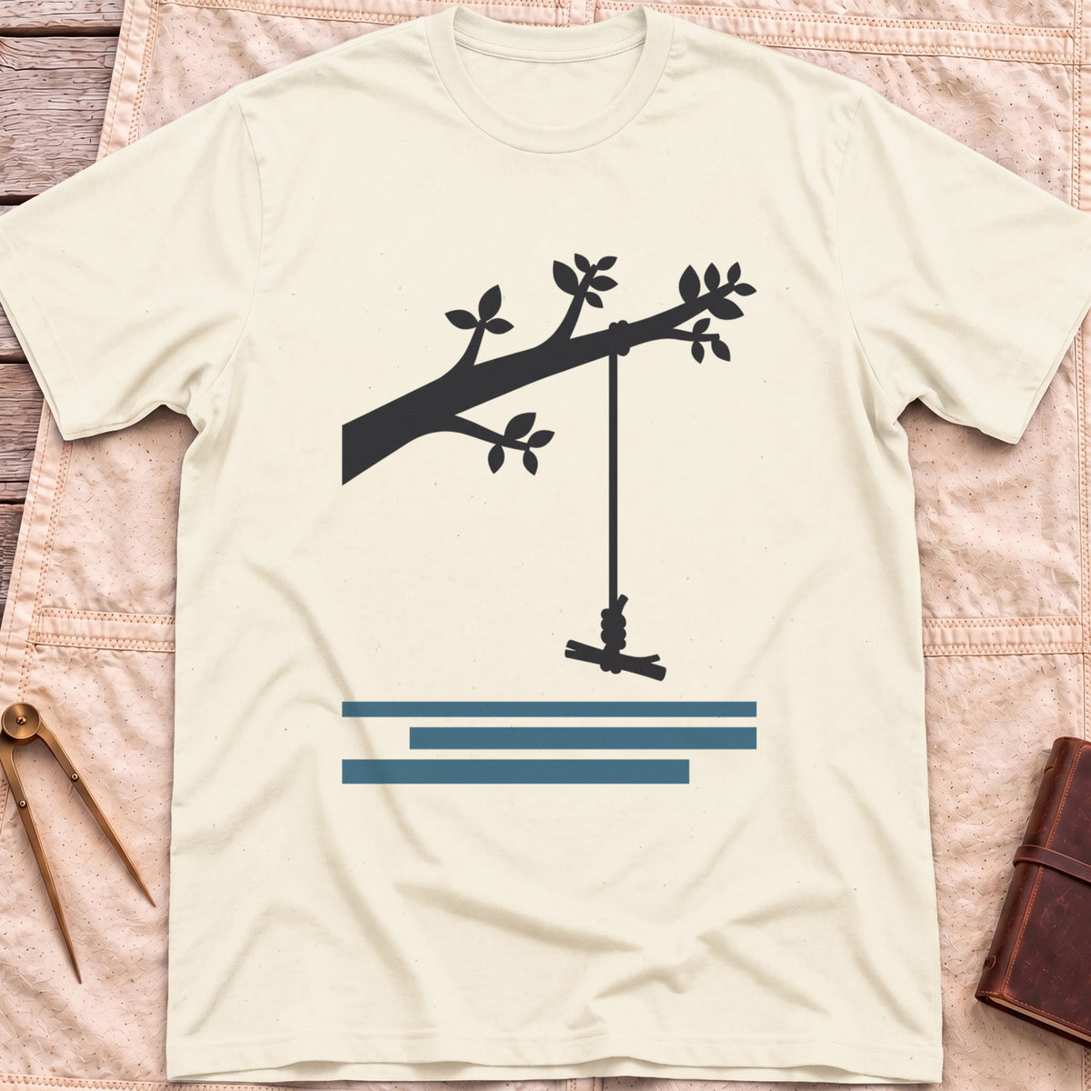 Front view of the natural Rope Swing T-Shirt with a rope swing hanging from a leafy branch above water lines.