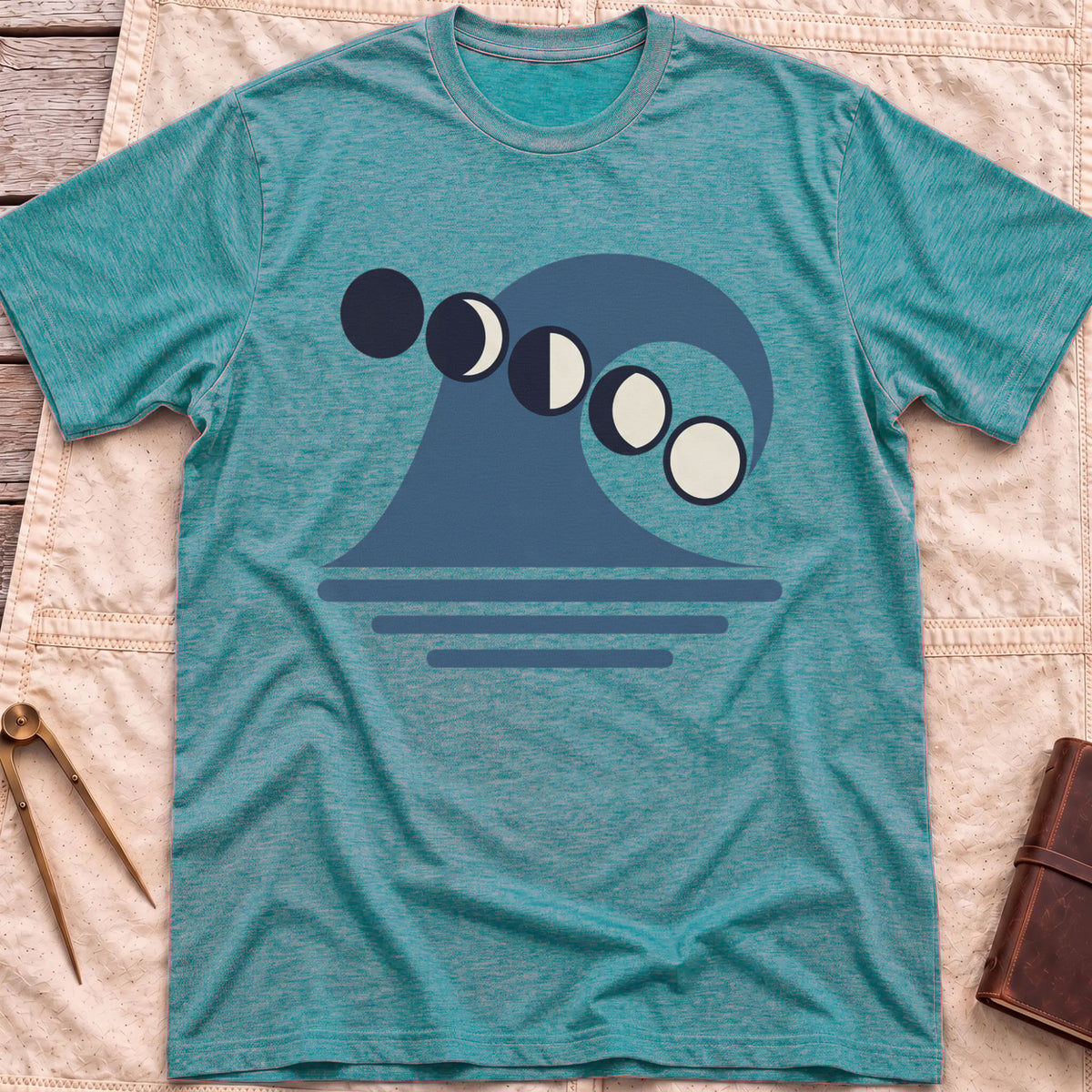 Front view of the heather galapagos blue Ruled by the Tides T-Shirt with a stylised wave, a row of moon phases and horizontal water lines.