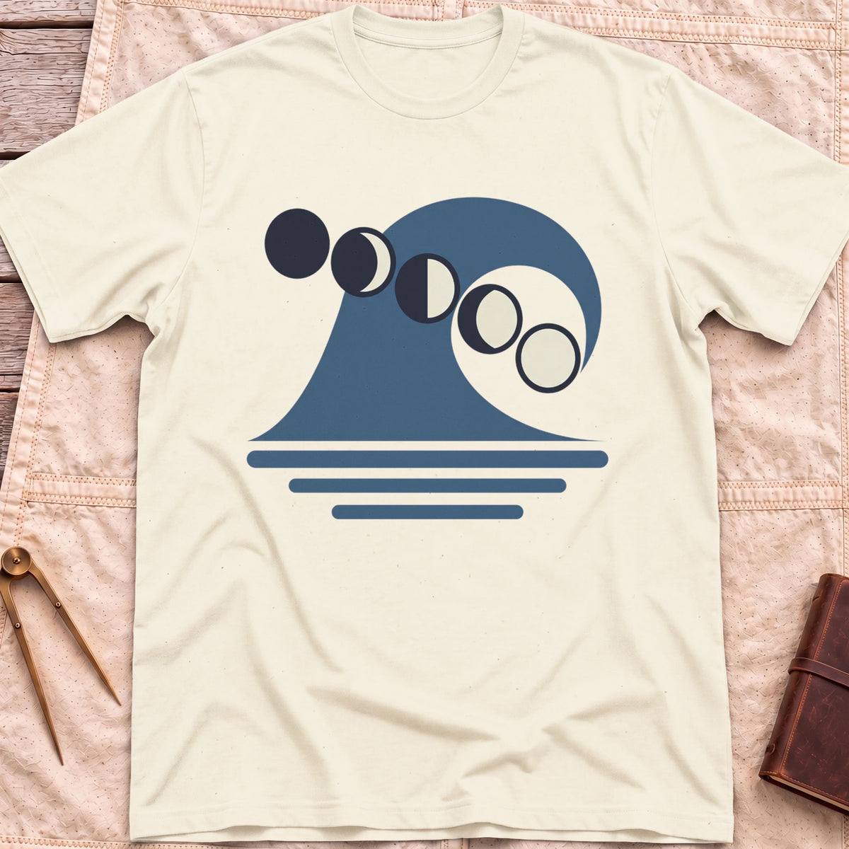 Front view of the natural Ruled by the Tides T-Shirt with a stylised wave, a row of moon phases and horizontal water lines.