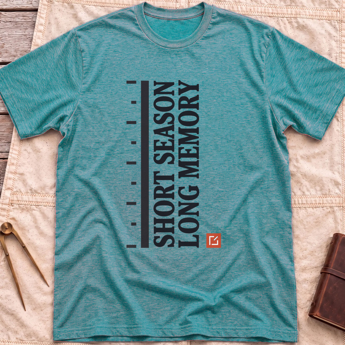 Front view of the heather galapagos blue Short Season Long Memory T-Shirt with the words Short Season Long Memory running vertically beside a tick-marked scale and a small red square.