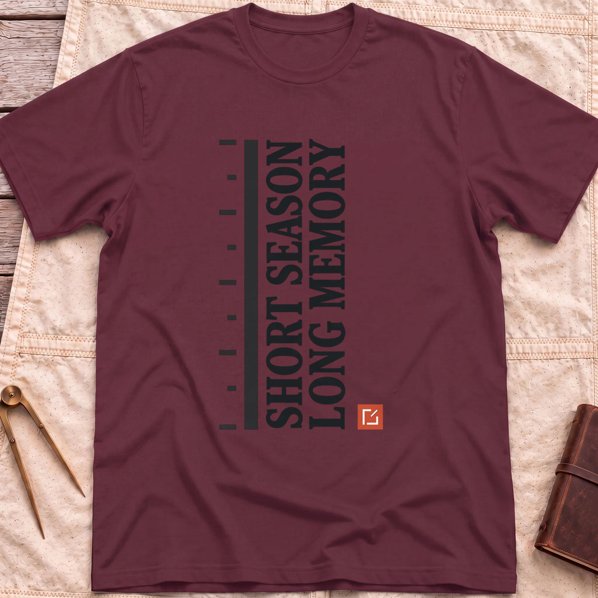 Front view of the maroon Short Season Long Memory T-Shirt with the words Short Season Long Memory running vertically beside a tick-marked scale and a small red square.