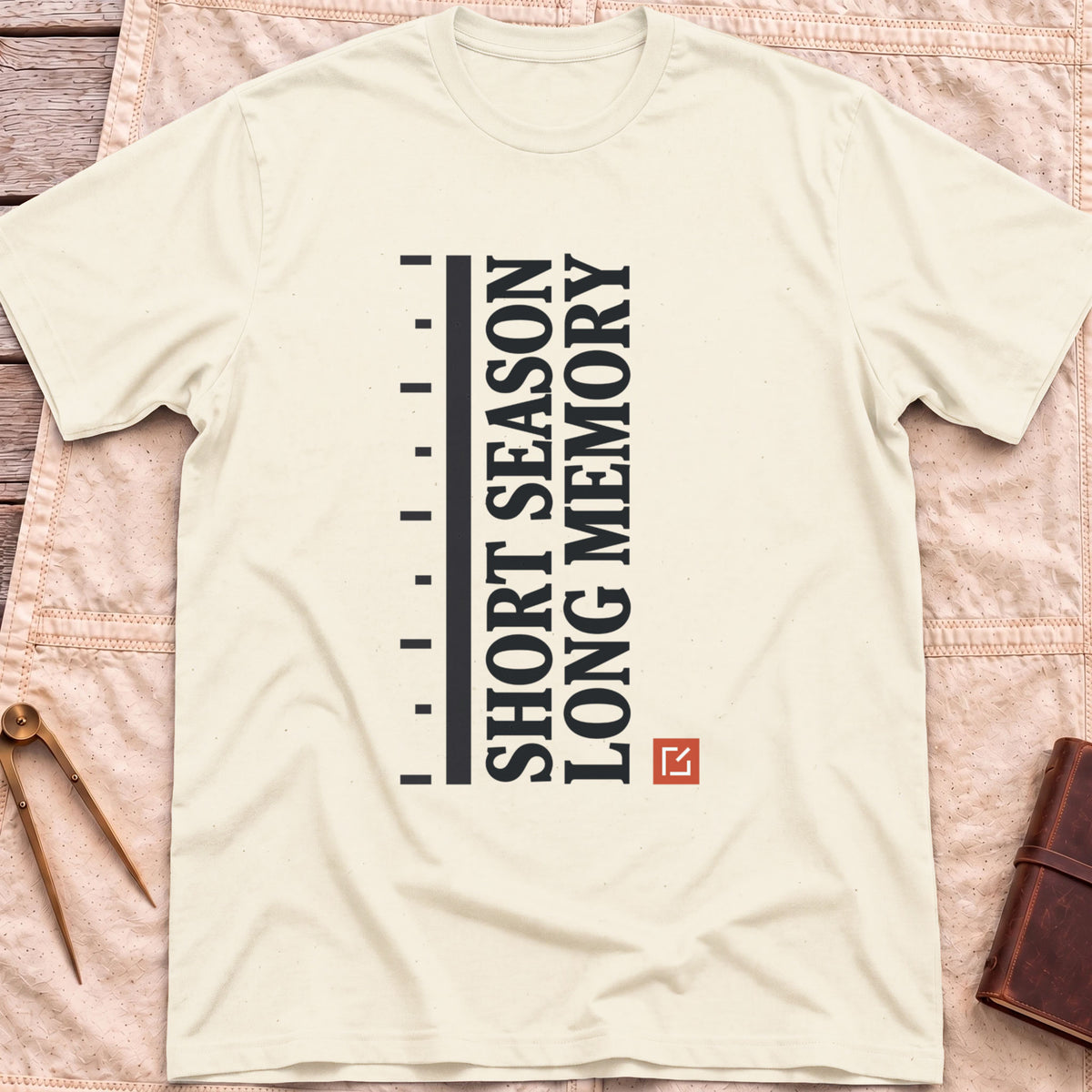 Front view of the natural Short Season Long Memory T-Shirt with the words Short Season Long Memory running vertically beside a tick-marked scale and a small red square.