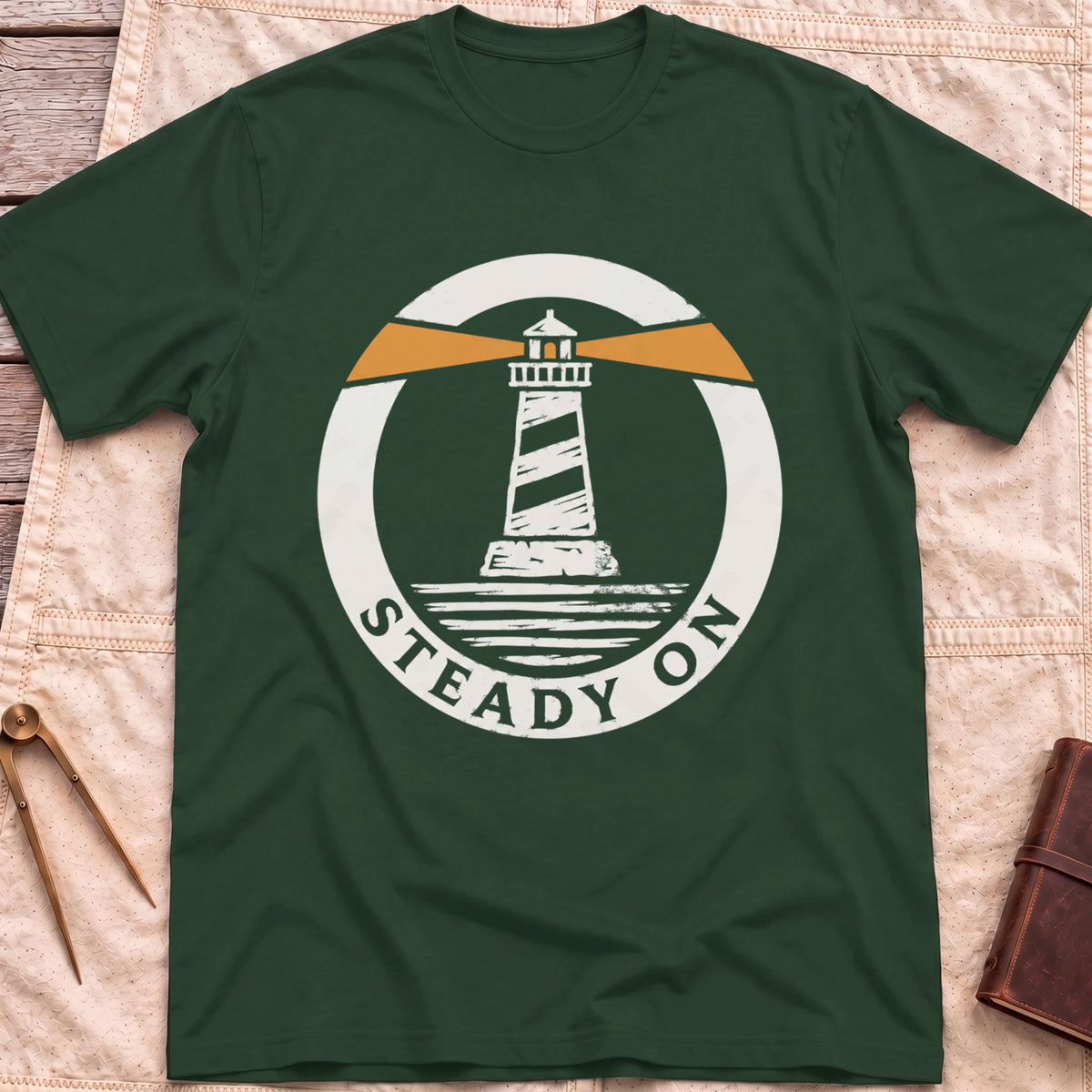 Front view of the forest green Steady On T-Shirt with a round badge showing a striped lighthouse and orange light beams over water.
