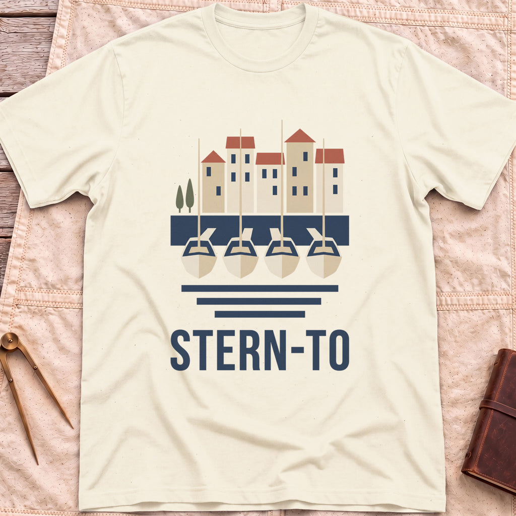 Front view of the natural Stern-To T-Shirt with four boats moored stern-first to a quay below a row of harbour houses, above the word Stern-To.