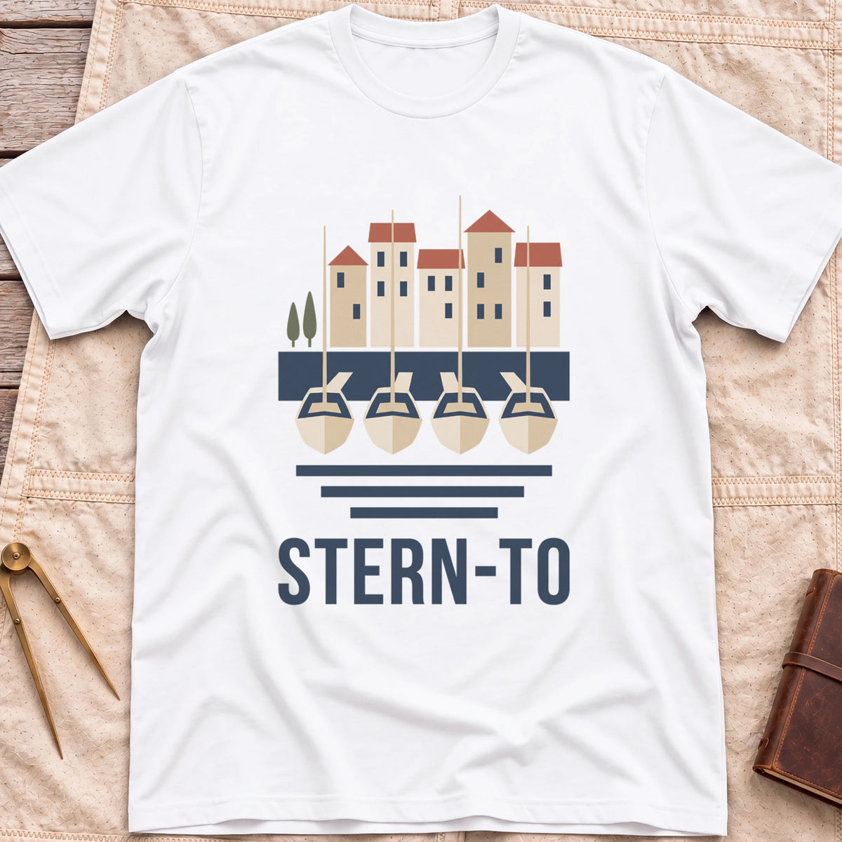 Front view of the white Stern-To T-Shirt with four boats moored stern-first to a quay below a row of harbour houses, above the word Stern-To.