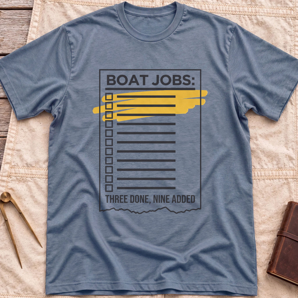 Front view of the heather indigo Still on the List T-Shirt with a Boat Jobs checklist, its top items highlighted in yellow, above the words Three Done, Nine Added.