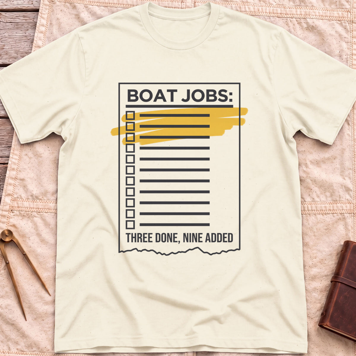 Front view of the natural Still on the List T-Shirt with a Boat Jobs checklist, its top items highlighted in yellow, above the words Three Done, Nine Added.