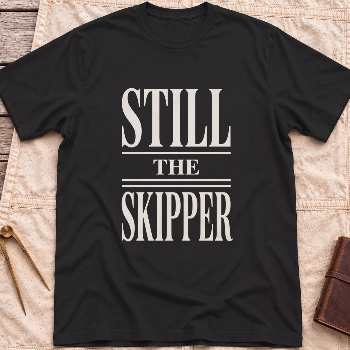 Front view of the black Still the Skipper T-Shirt with the words Still the Skipper in cream serif capitals.