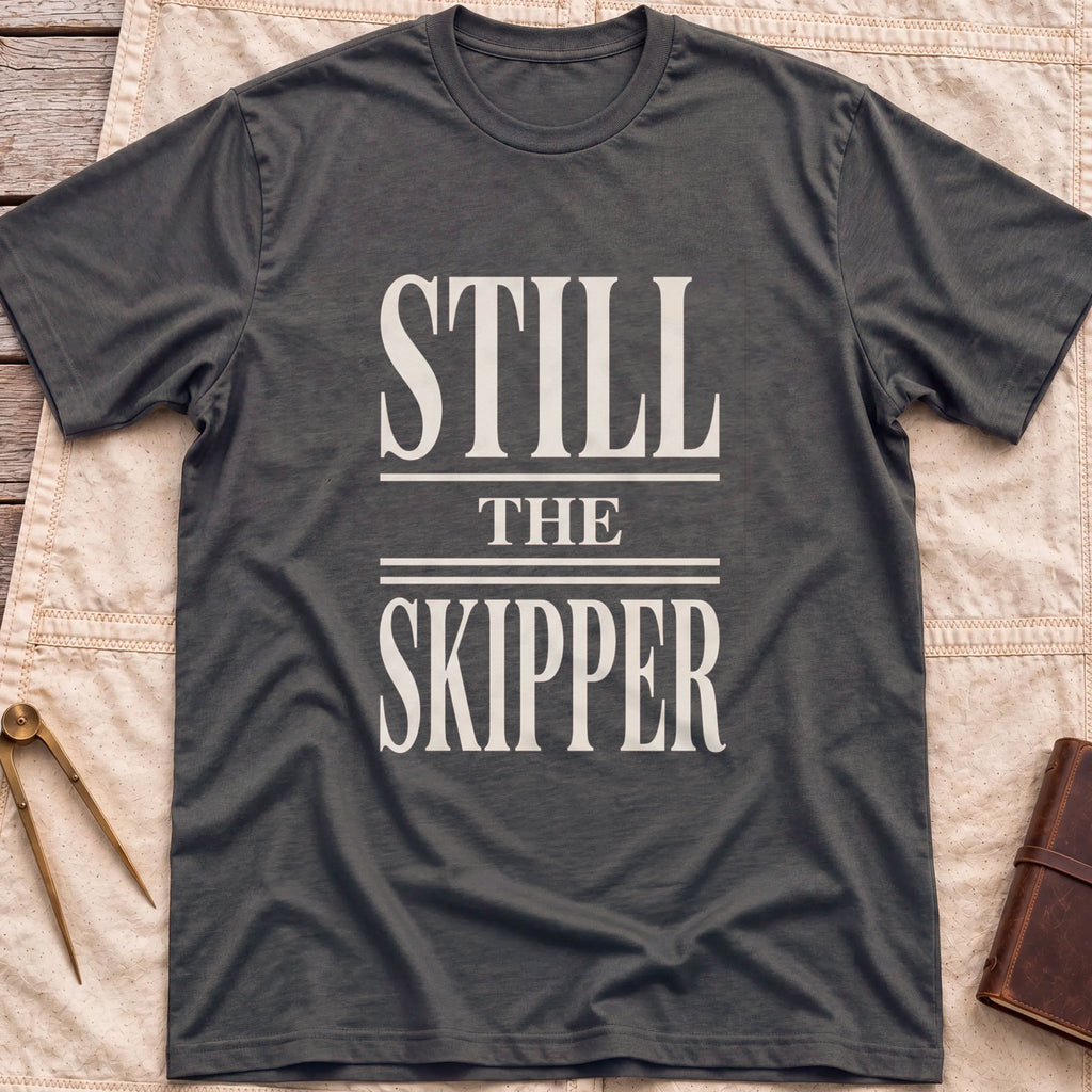 Front view of the dark heather Still the Skipper T-Shirt with the words Still the Skipper in cream serif capitals.
