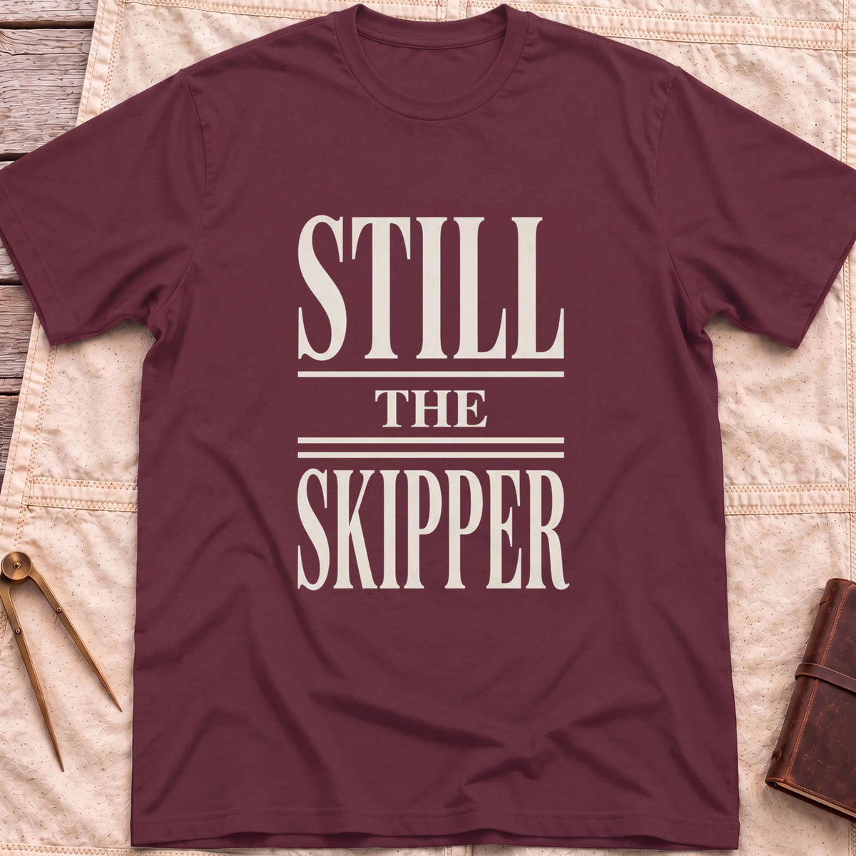 Front view of the maroon Still the Skipper T-Shirt with the words Still the Skipper in cream serif capitals.