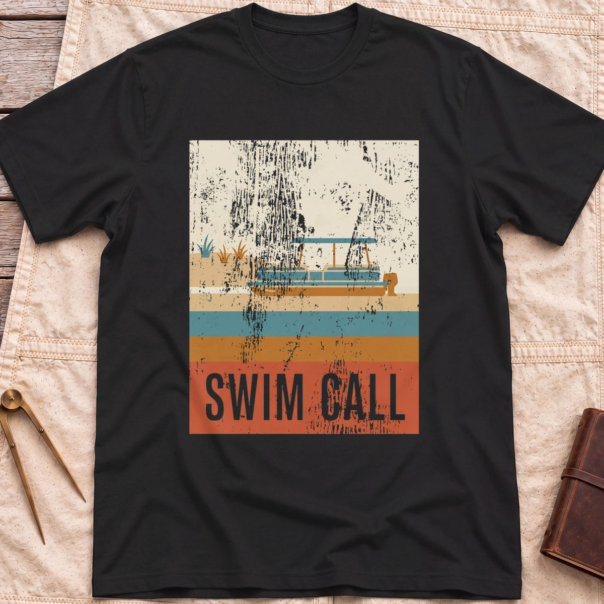 Front view of the black Swim Call T-Shirt with a distressed retro poster of a canopied pontoon boat over striped water above the words Swim Call.