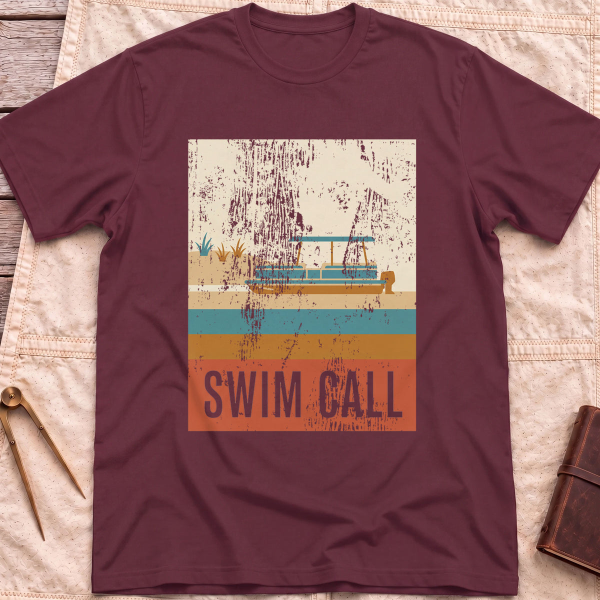 Front view of the maroon Swim Call T-Shirt with a distressed retro poster of a canopied pontoon boat over striped water above the words Swim Call.