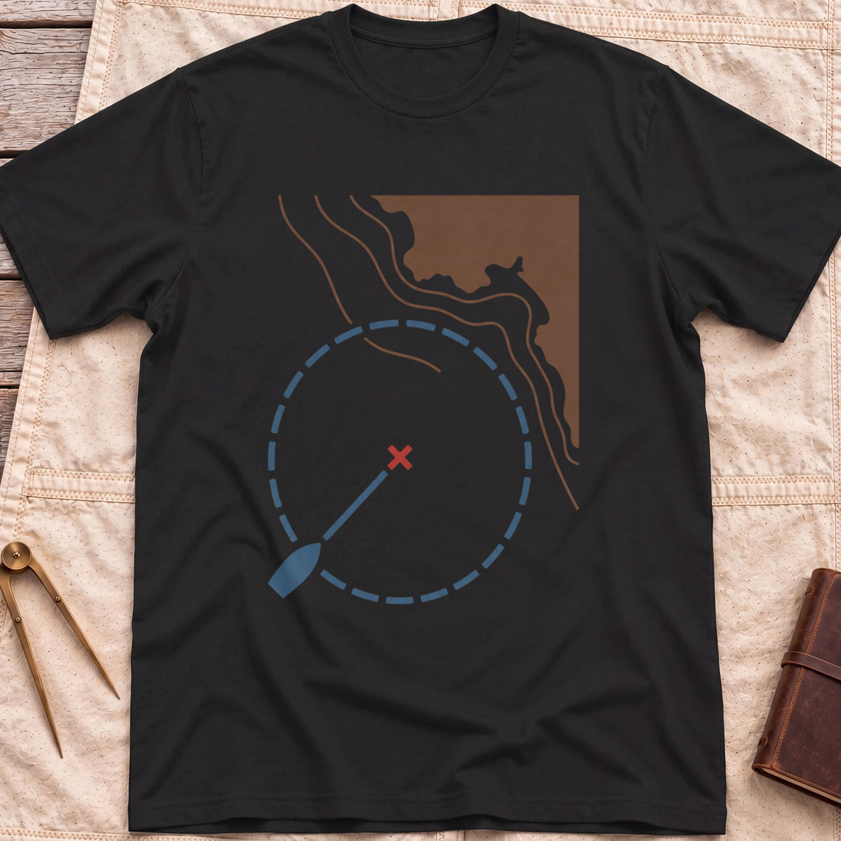 Front view of the black Swing Circle T-Shirt with a boat on a line inside a dashed circle around a red cross, beside a stretch of coastline.