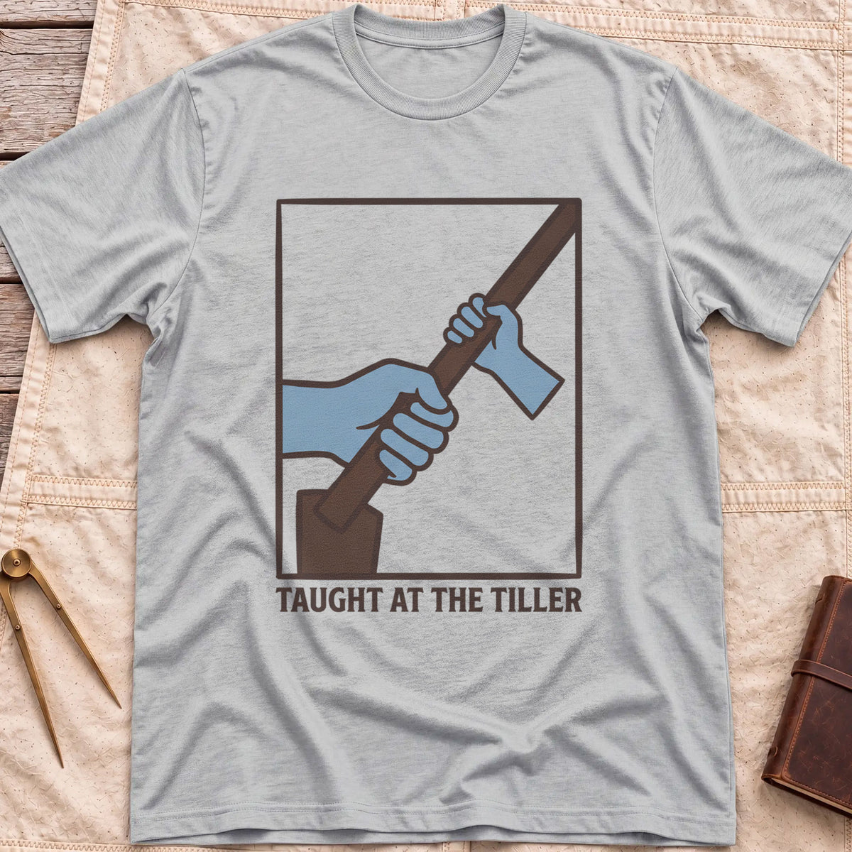 Front view of the sport grey Taught at the Tiller T-Shirt with a framed illustration of a larger hand and a smaller hand gripping a tiller together.