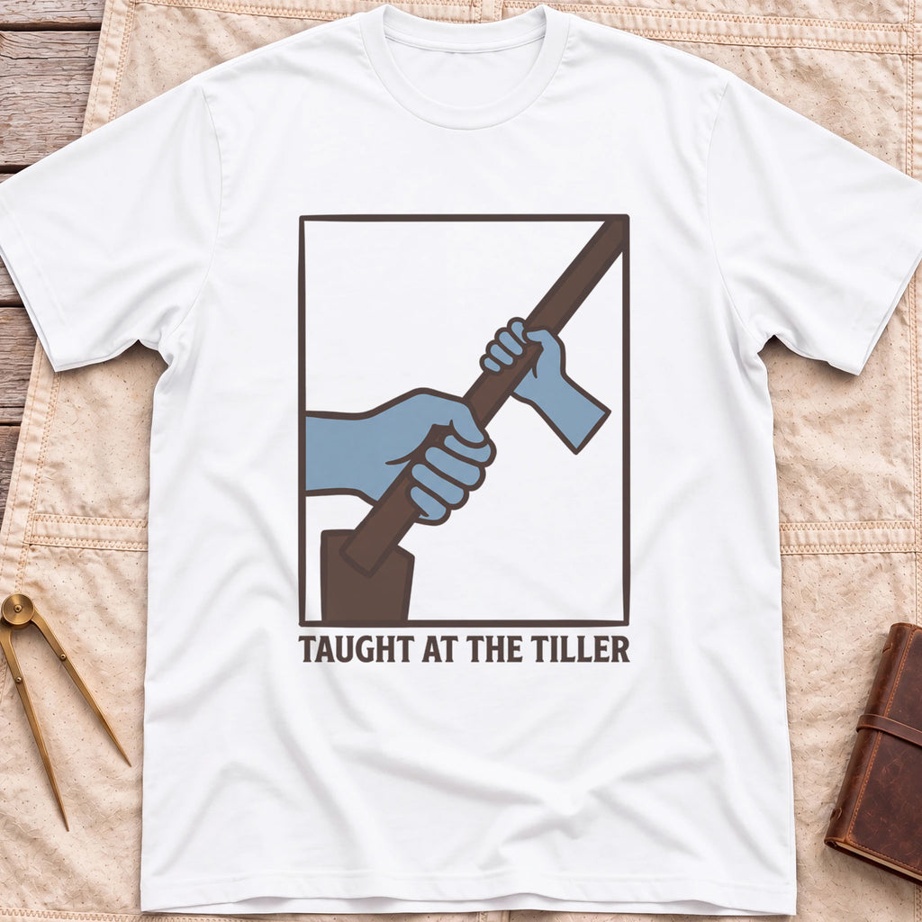 Front view of the white Taught at the Tiller T-Shirt with a framed illustration of a larger hand and a smaller hand gripping a tiller together.