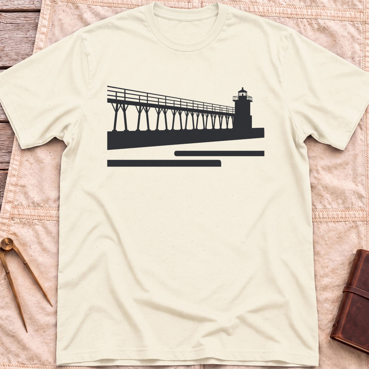 Front view of the natural The Catwalk T-Shirt with a silhouette of a raised walkway running along a pier to a lighthouse.