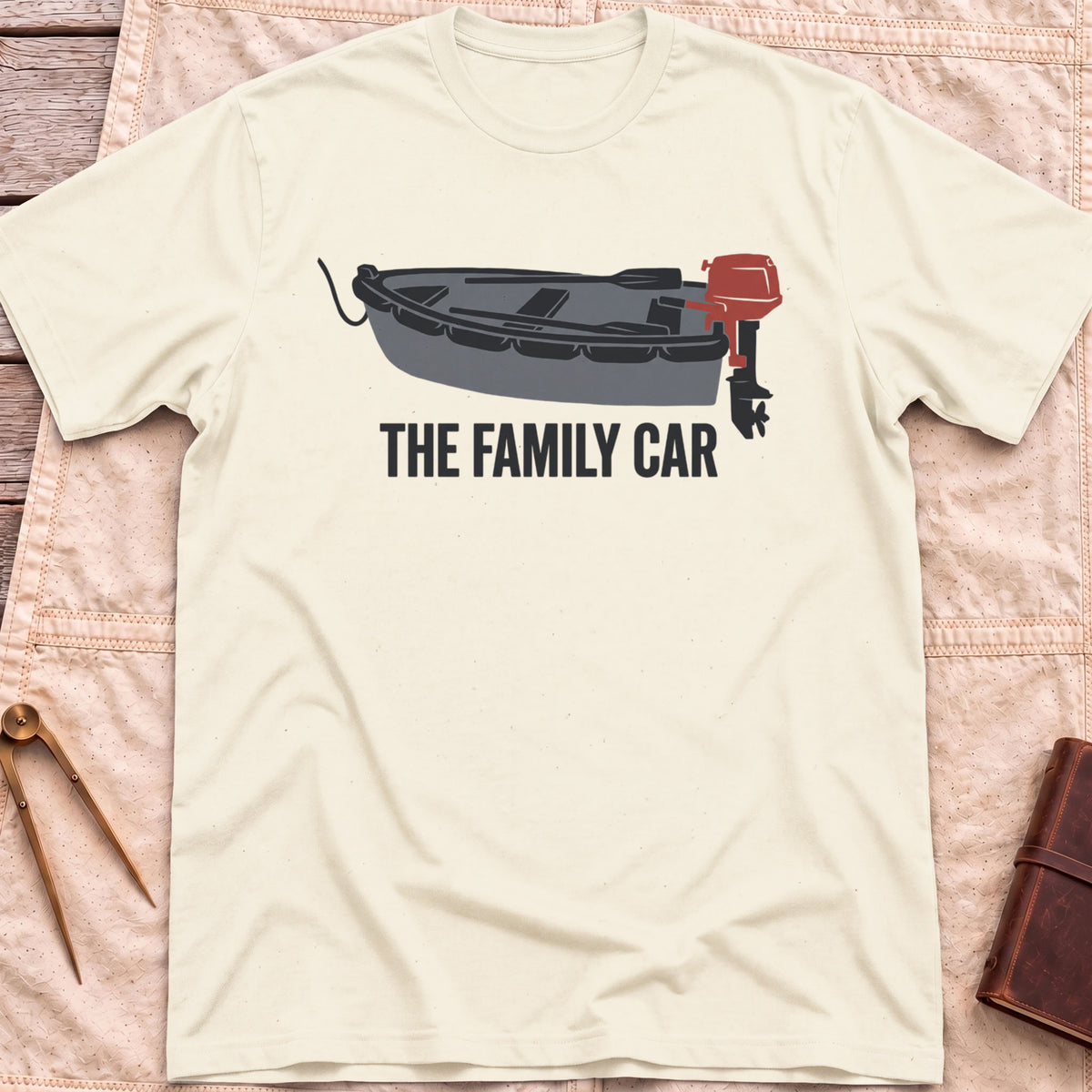 Front view of the natural The Family Car T-Shirt with a small open boat fitted with a red outboard motor.