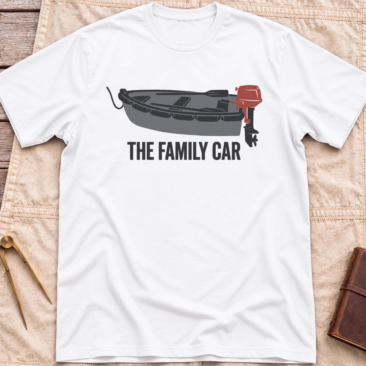 Front view of the white The Family Car T-Shirt with a small open boat fitted with a red outboard motor.