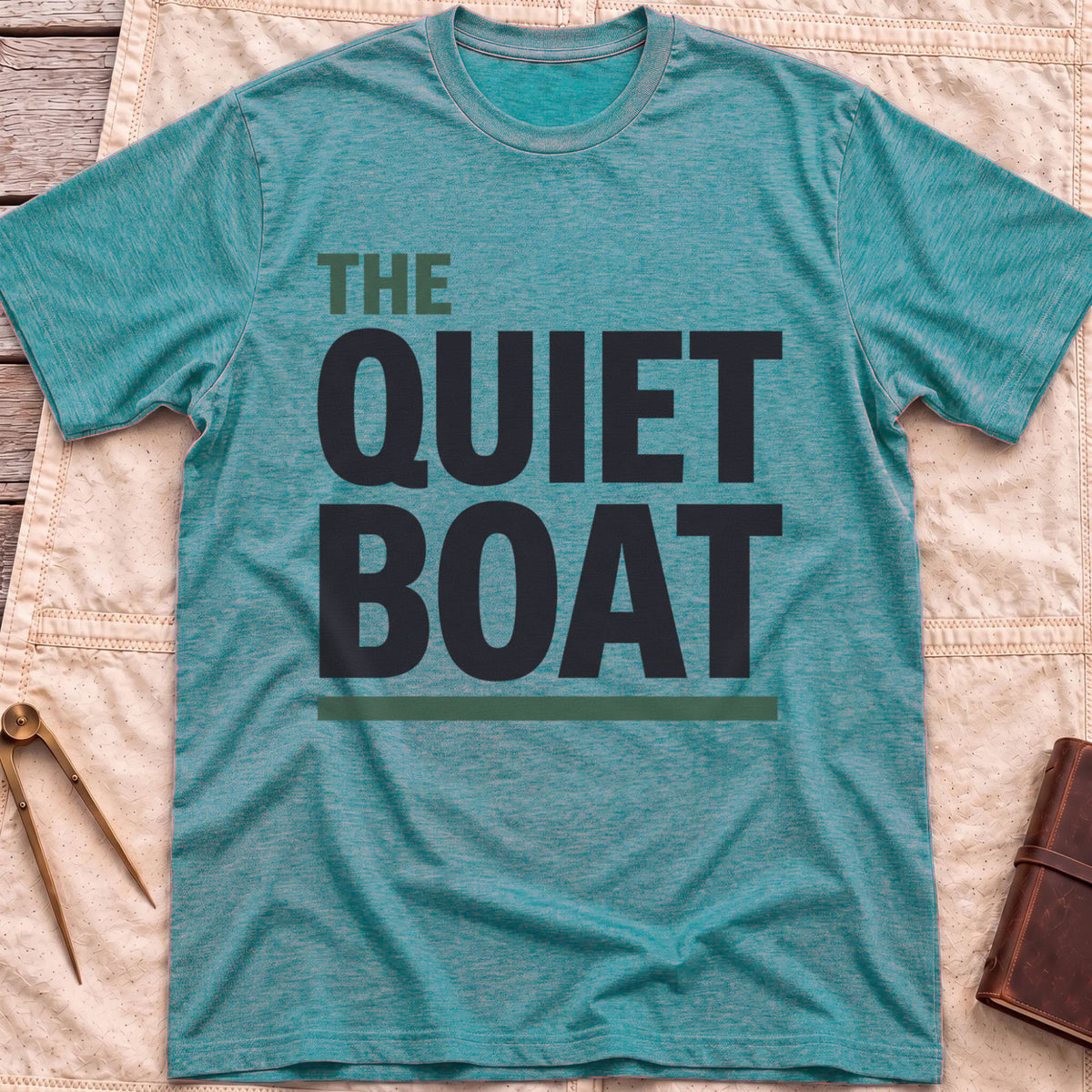 Front view of the heather galapagos blue The Quiet Boat T-Shirt with the words The Quiet Boat in heavy capitals above a green underline.