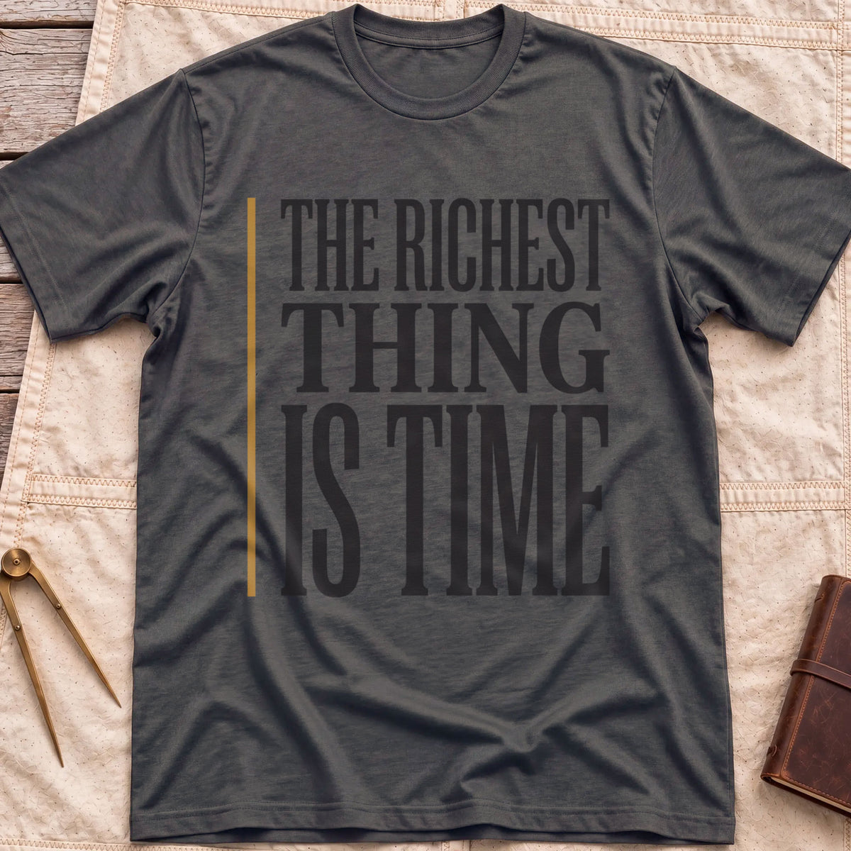 Front view of the dark heather The Richest Thing T-Shirt with the words The Richest Thing Is Time in tall condensed type beside a tan line.