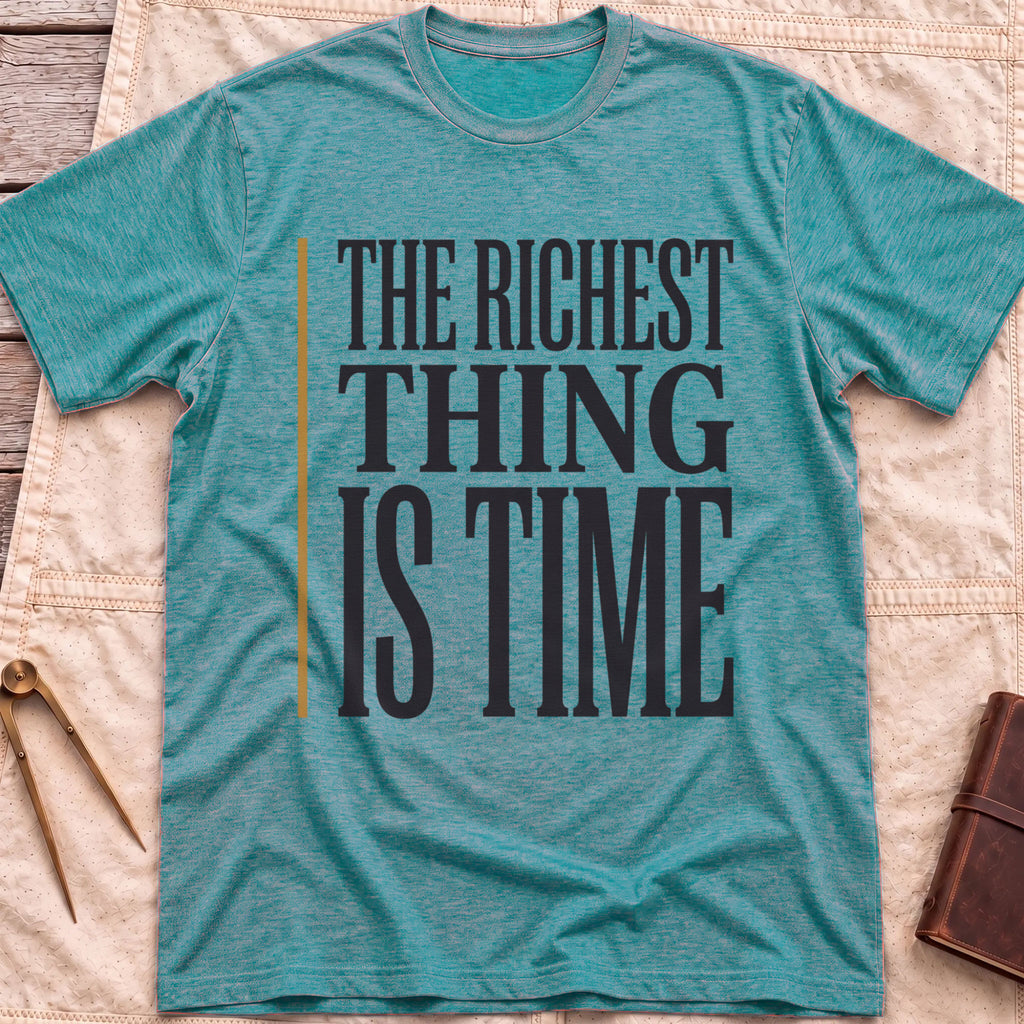 Front view of the heather galapagos blue The Richest Thing T-Shirt with the words The Richest Thing Is Time in tall condensed type beside a tan line.