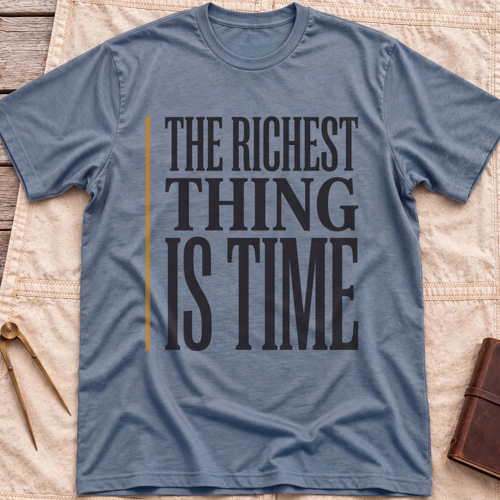 Front view of the heather indigo The Richest Thing T-Shirt with the words The Richest Thing Is Time in tall condensed type beside a tan line.