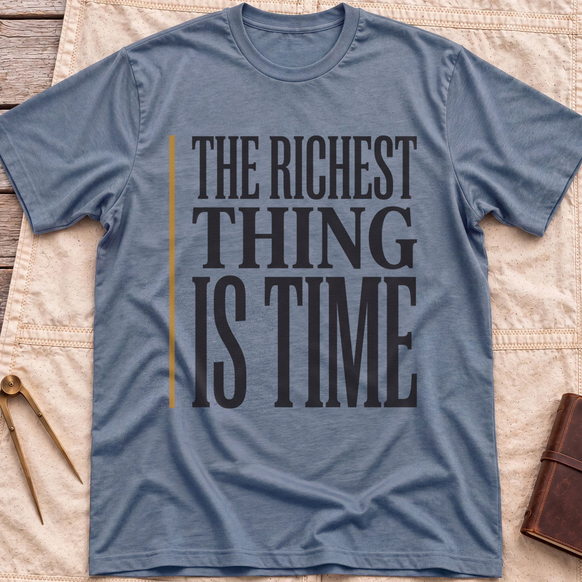 Front view of the heather indigo The Richest Thing T-Shirt with the words The Richest Thing Is Time in tall condensed type beside a tan line.