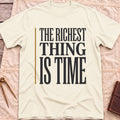 Front view of the natural The Richest Thing T-Shirt with the words The Richest Thing Is Time in tall condensed type beside a tan line.