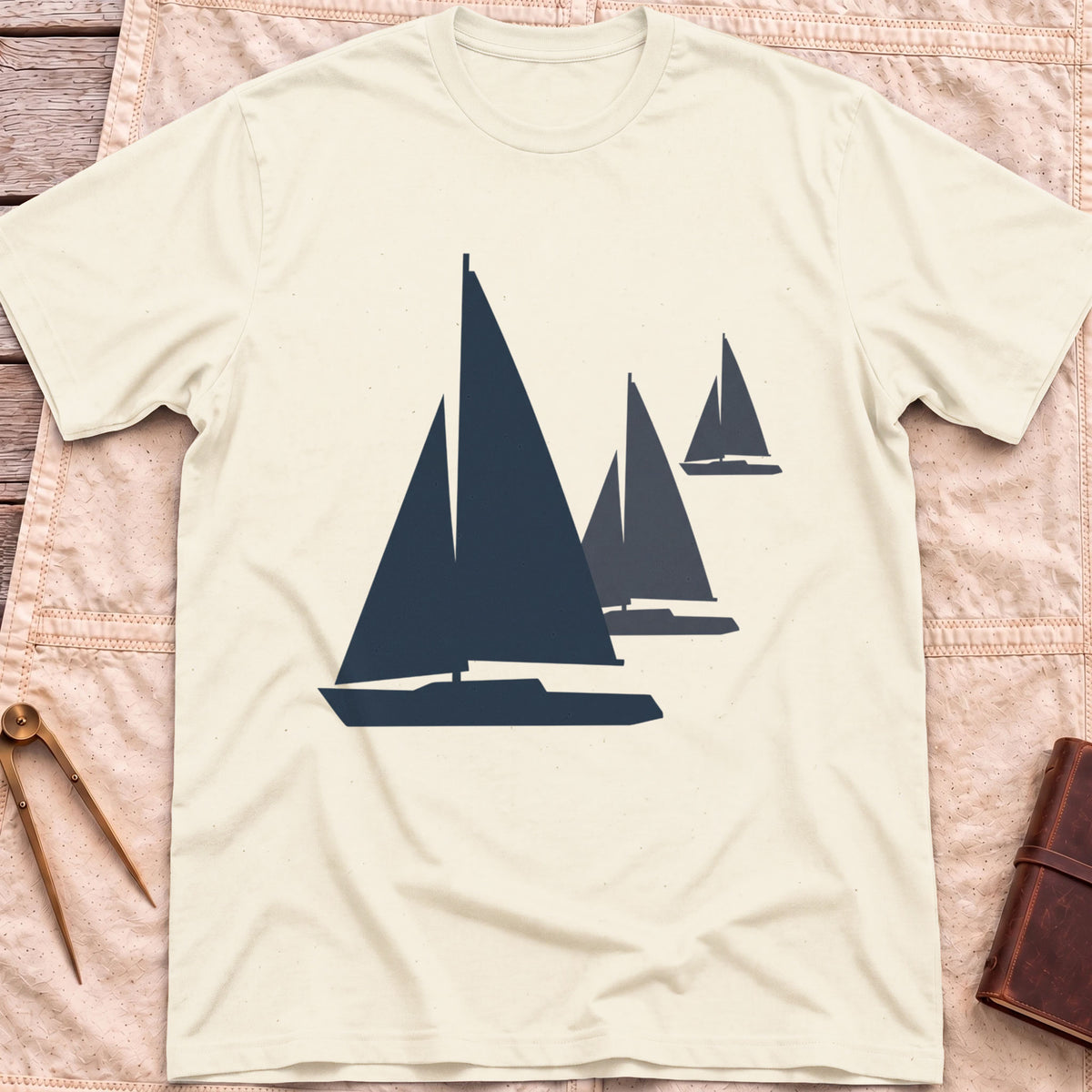Front view of the natural Three Sails T-Shirt with silhouettes of three sailboats in decreasing sizes.