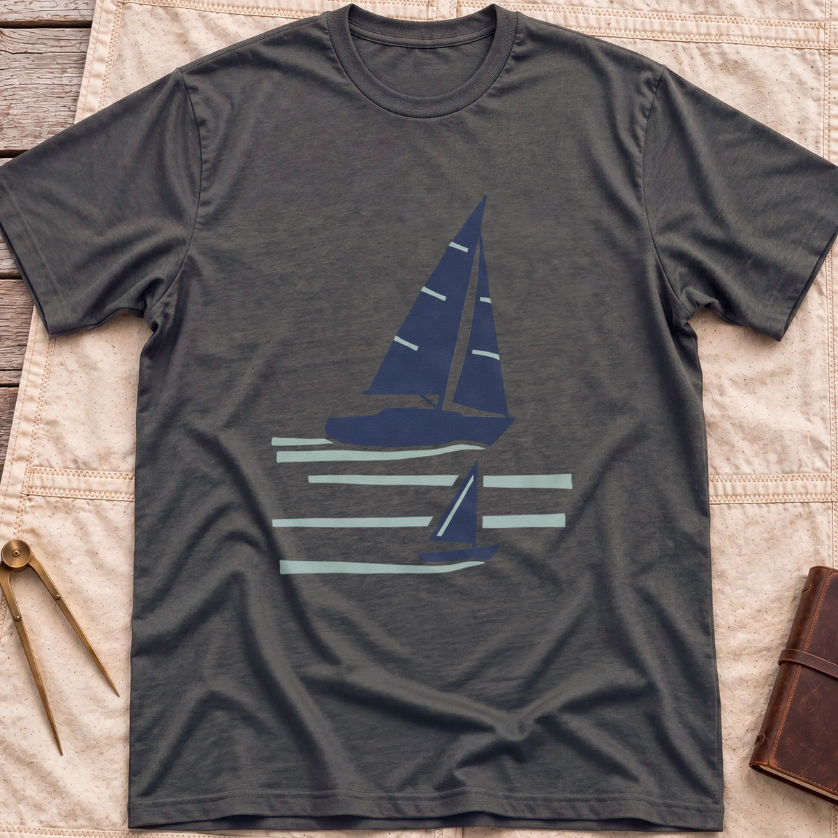 Front view of the dark heather Two Wake T-Shirt with a large and a small sailboat over pale wake lines.
