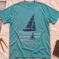 Front view of the heather galapagos blue Two Wake T-Shirt with a large and a small sailboat over pale wake lines.