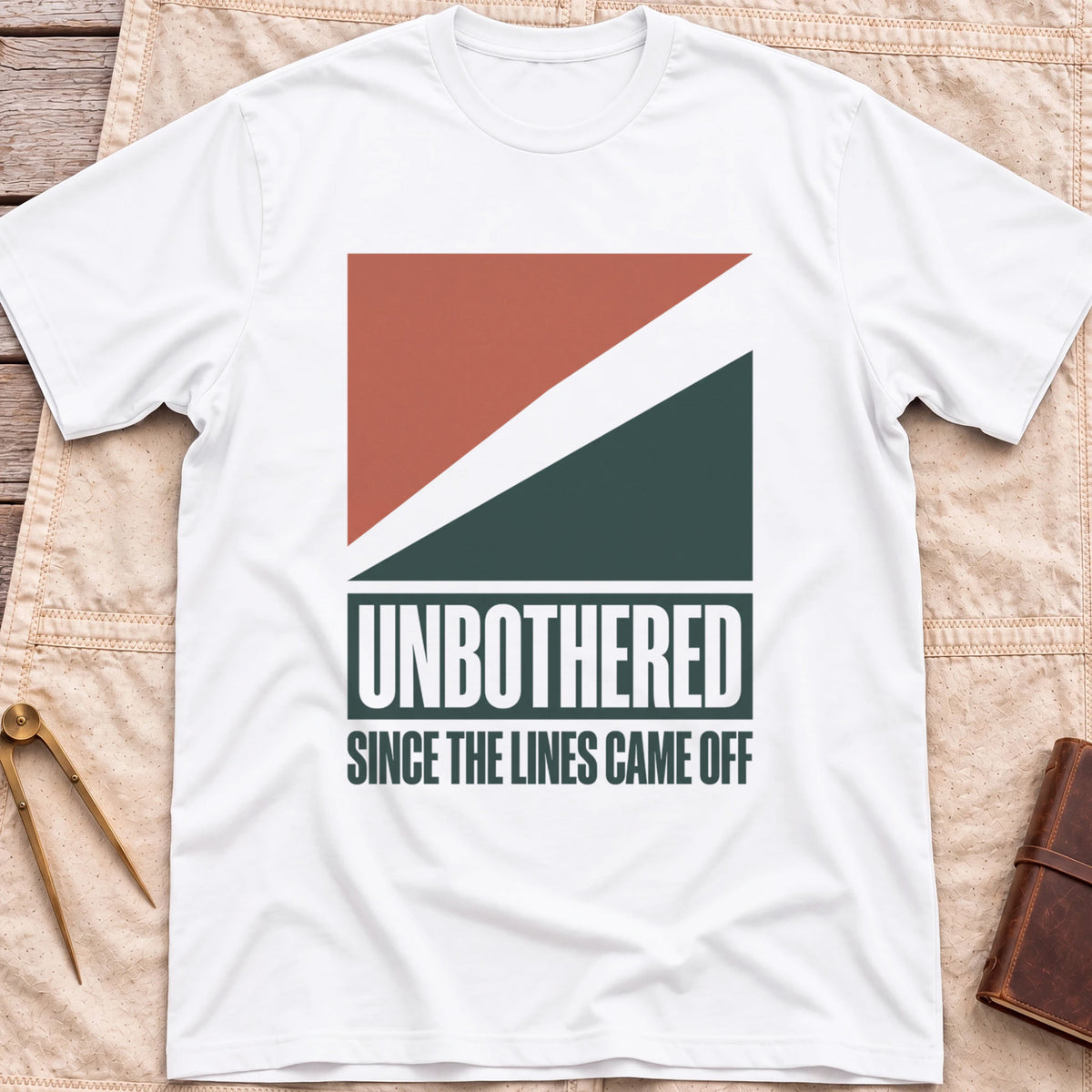 Front view of the white Unbothered T-Shirt with rust-red and dark green diagonal blocks above the words Unbothered, Since the Lines Came Off.