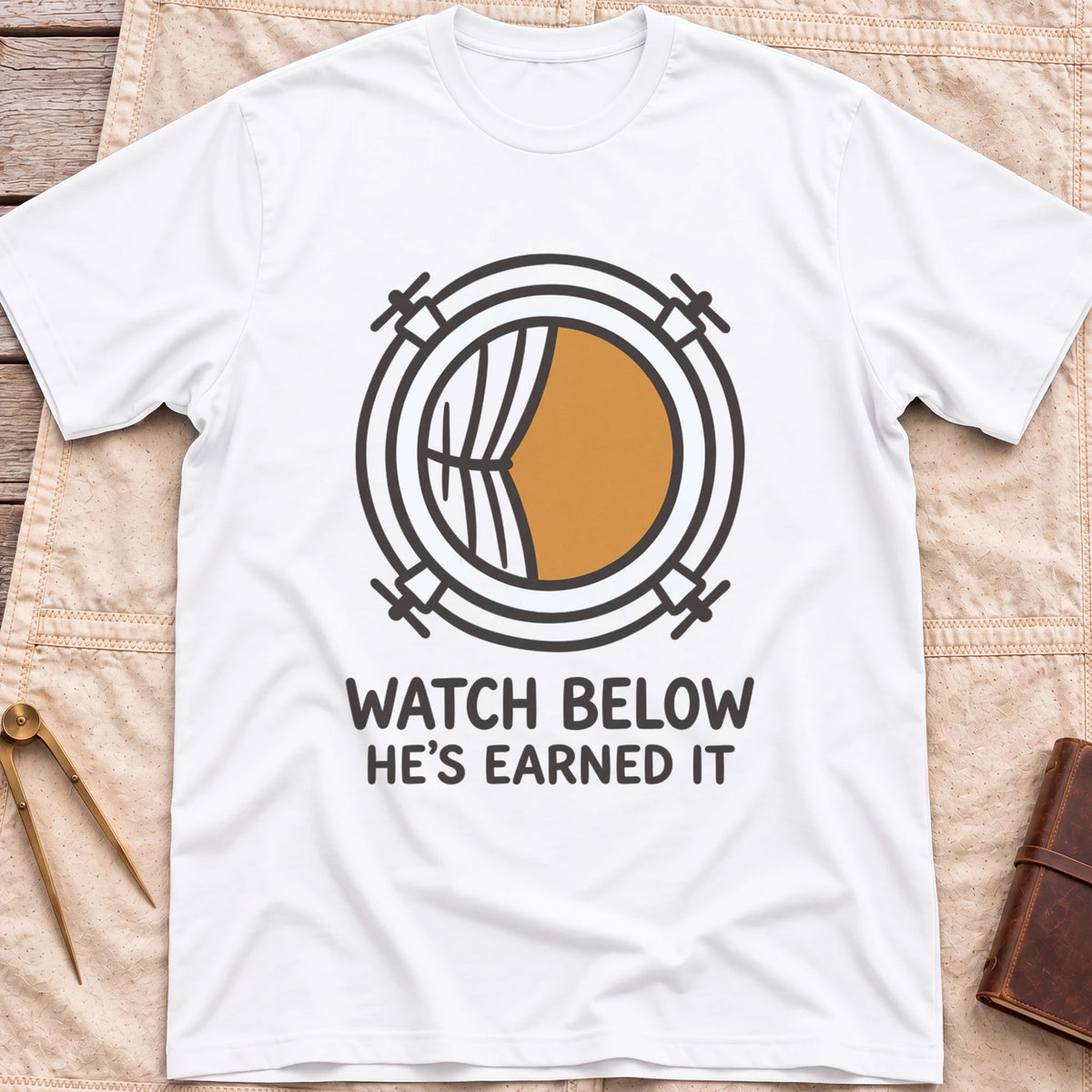 Front view of the white Watch Below T-Shirt with a round porthole and a half-drawn curtain above the words He's Earned It.