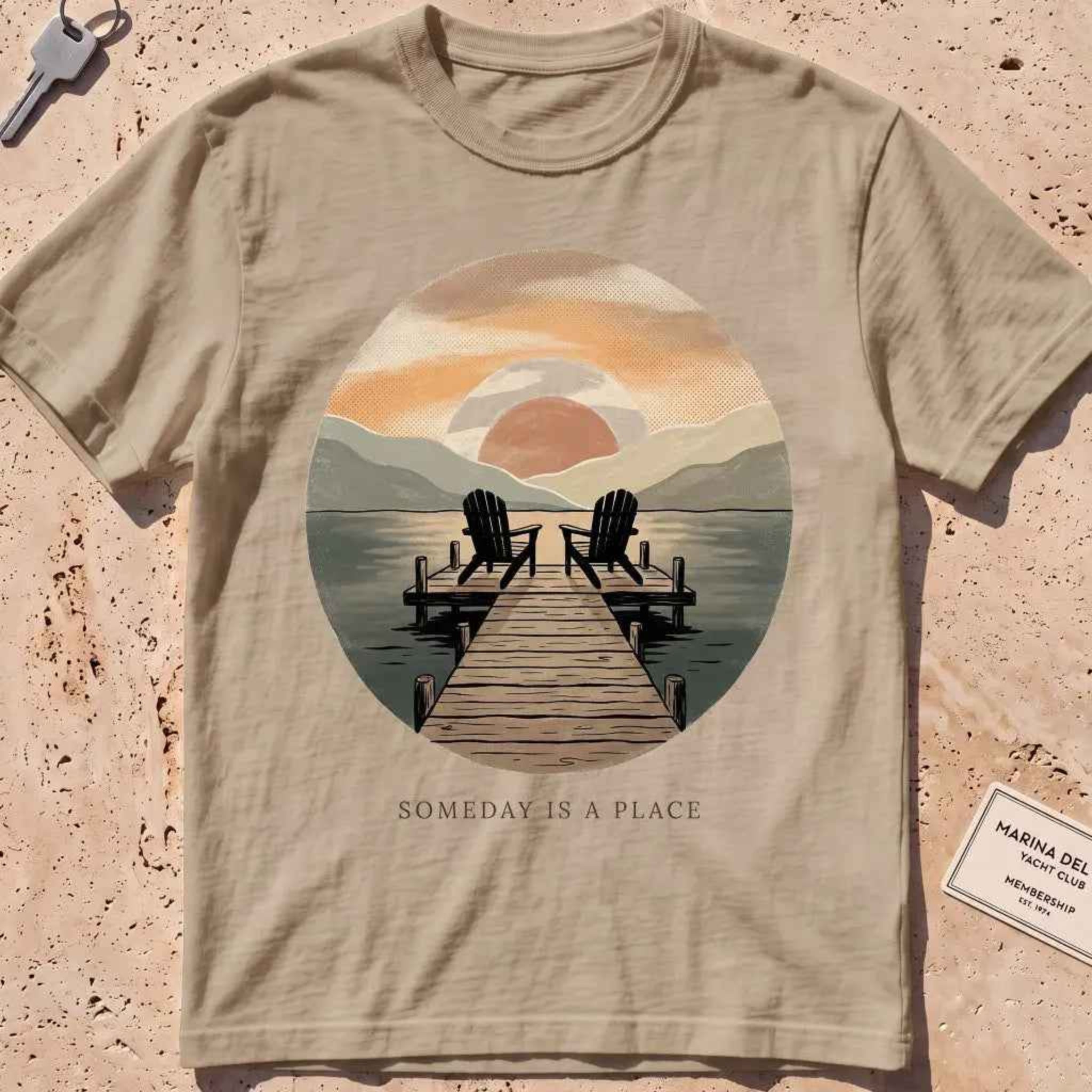 khaki heavyweight tee with a warm dock-at-dusk "Someday Is a Place" scene.