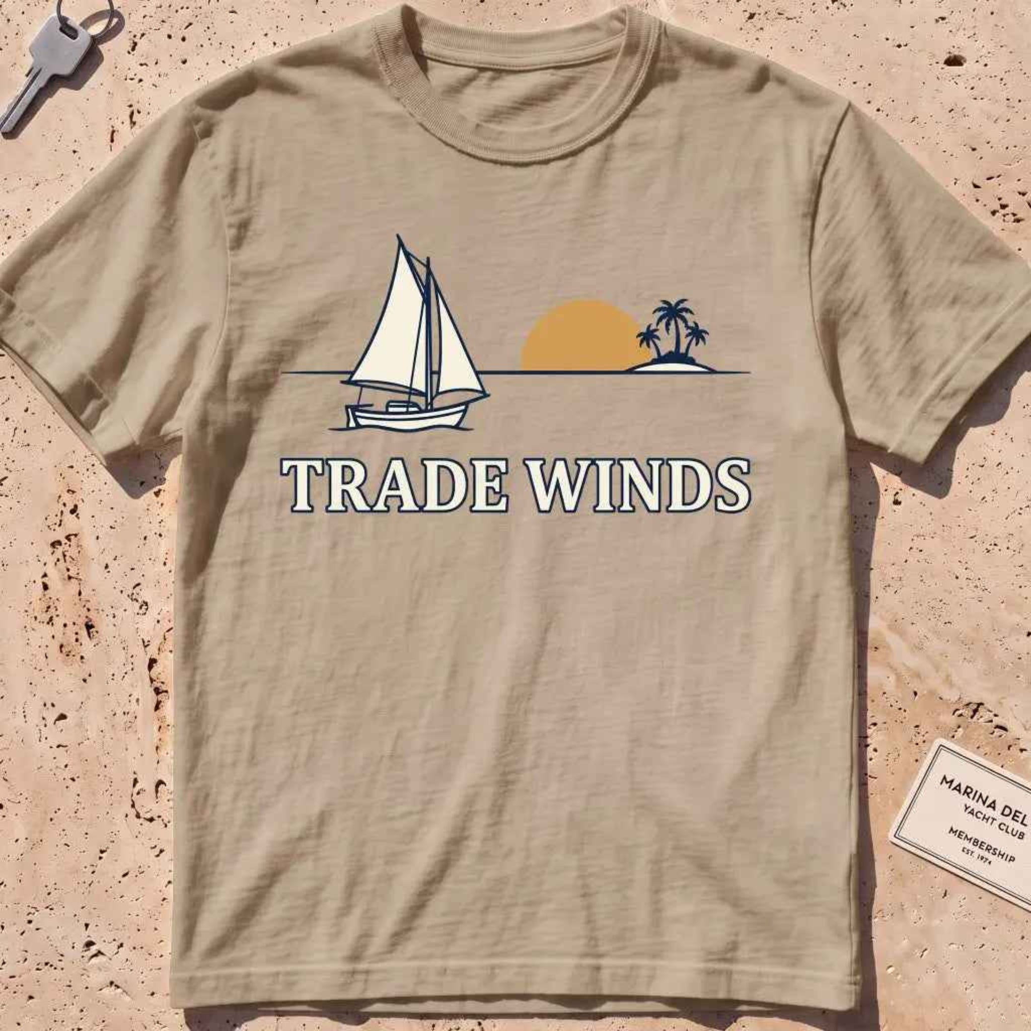 khaki heavyweight tee with a sailboat, sun and palms "Trade Winds" graphic.