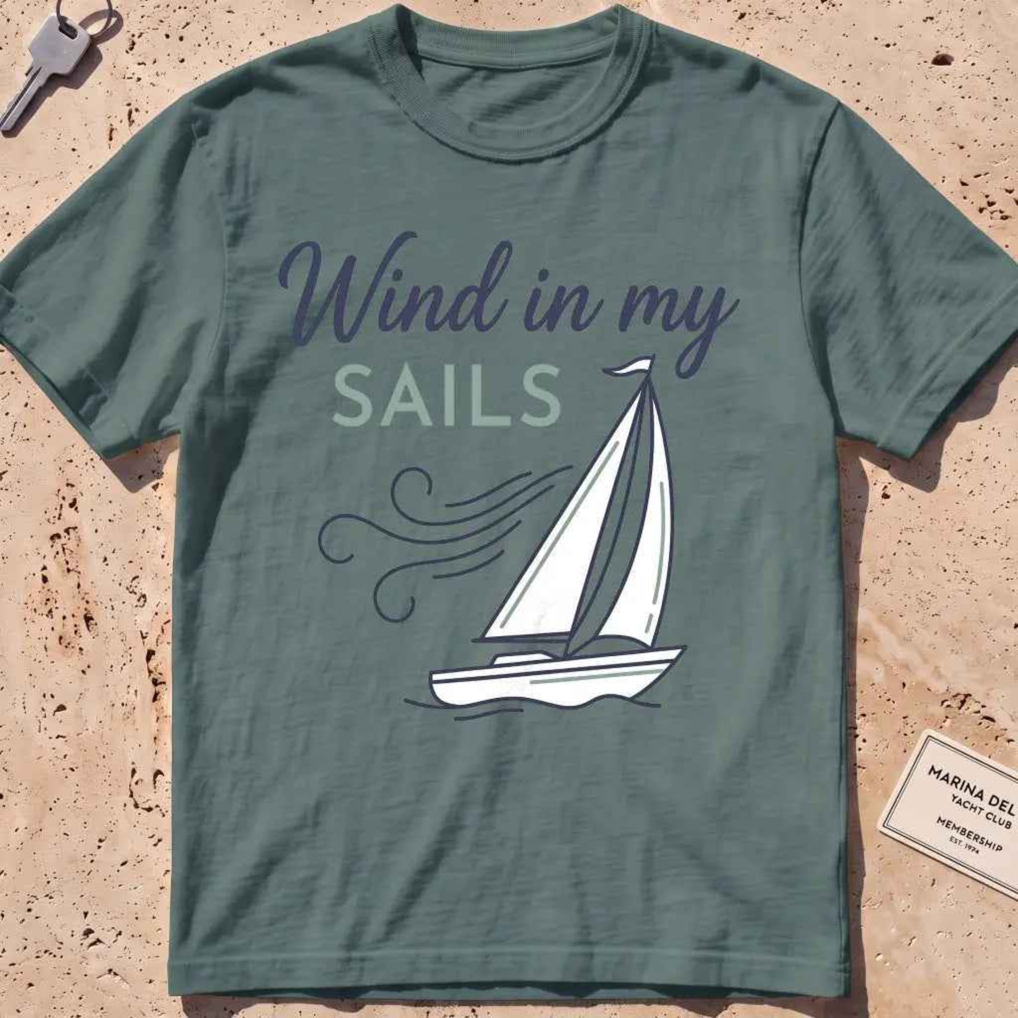 blue spruce heavyweight tee with a line-art sailboat "Wind in My Sails" graphic.