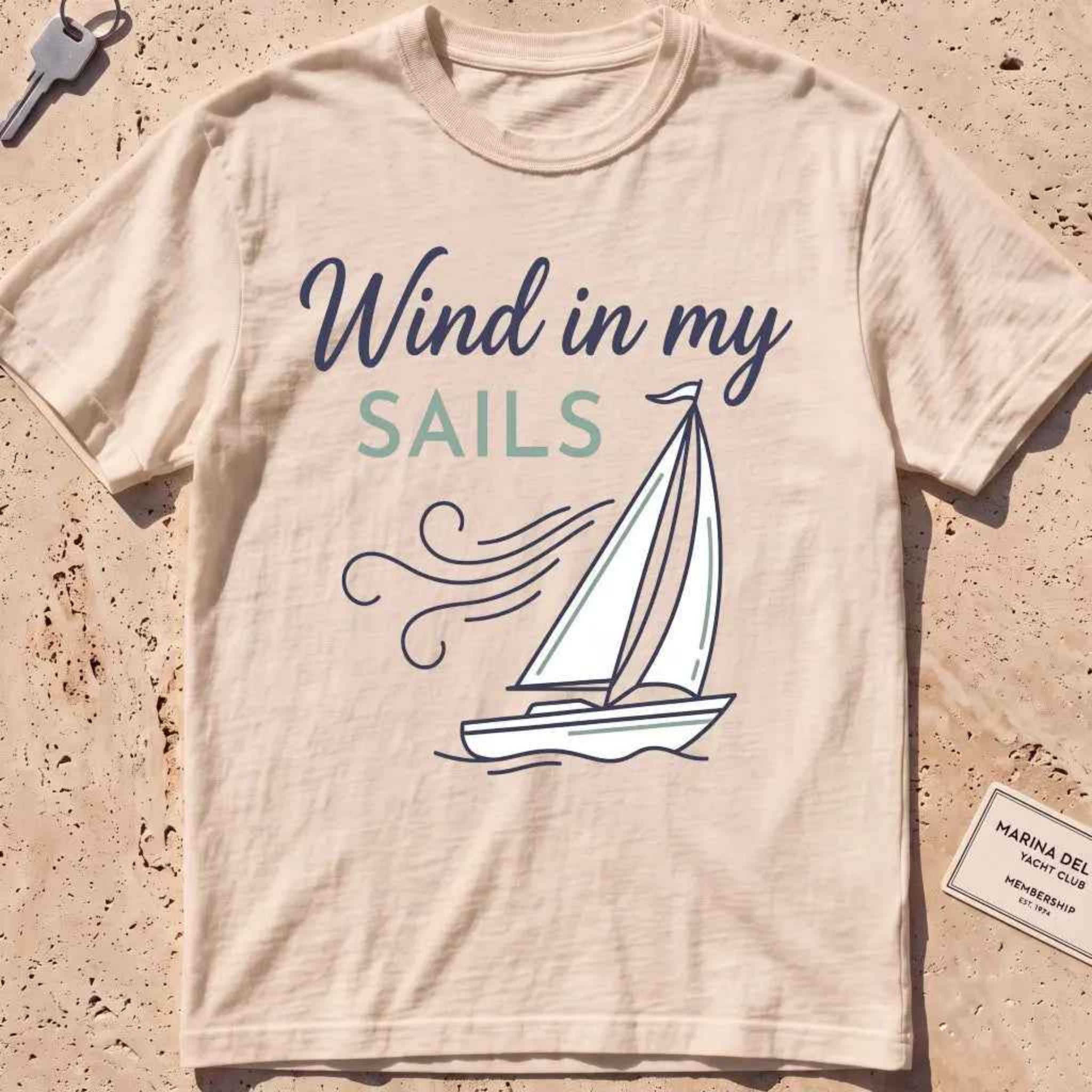 ivory heavyweight tee with a line-art sailboat "Wind in My Sails" graphic.