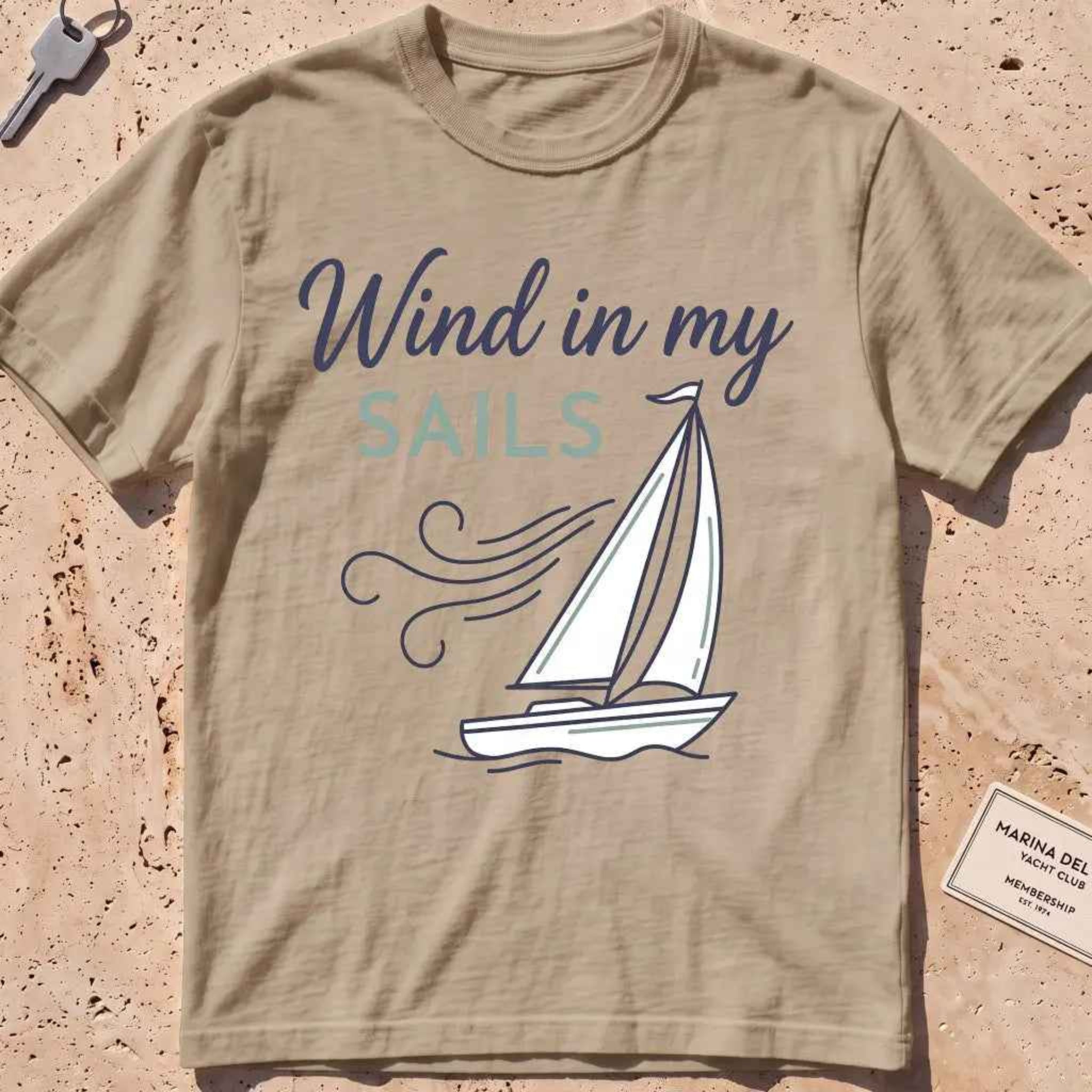 khaki heavyweight tee with a line-art sailboat "Wind in My Sails" graphic.