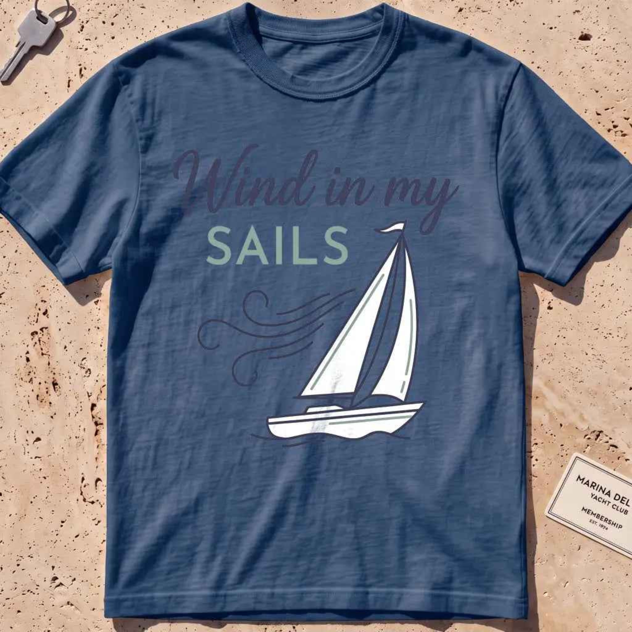 midnight heavyweight tee with a line-art sailboat "Wind in My Sails" graphic.